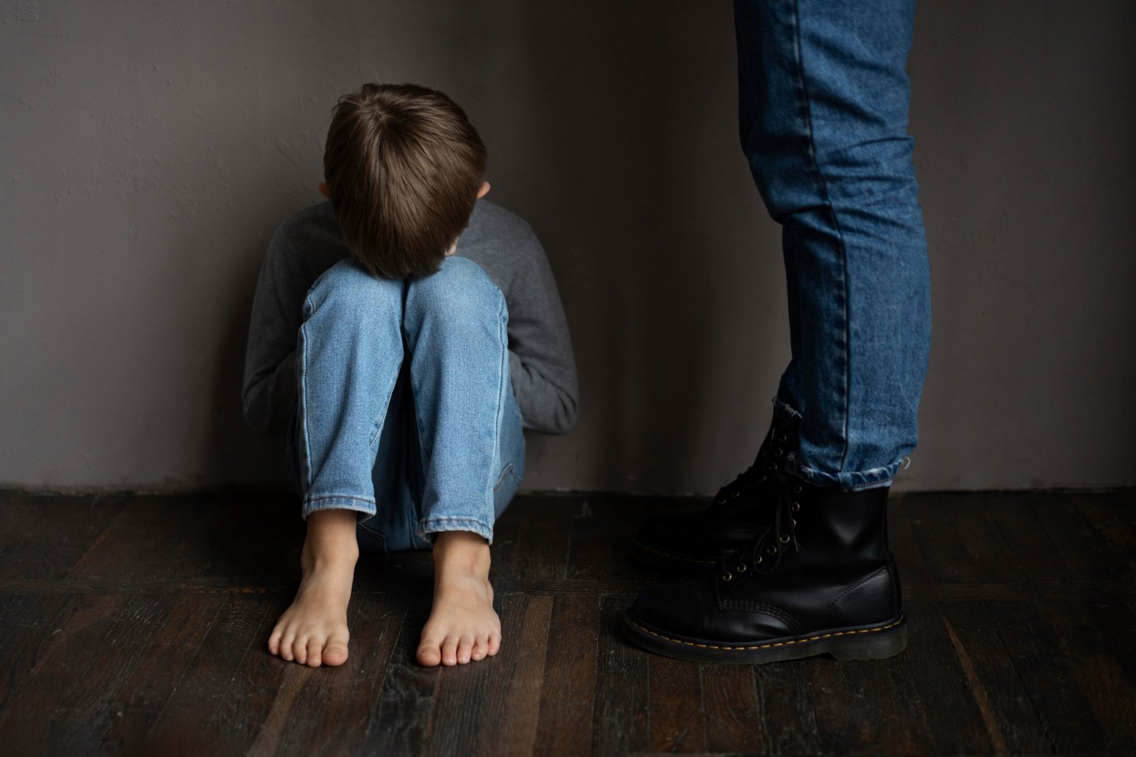 Child sitting on the floor with an adult standing nearby