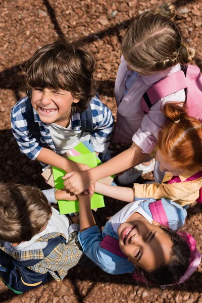 Children stacking hands together above books